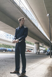 Businessman standing at underpass holding laptop - KNSF02480