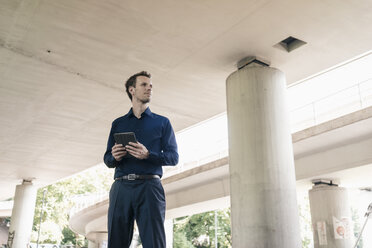 Businessman standing at underpass holding tablet - KNSF02483