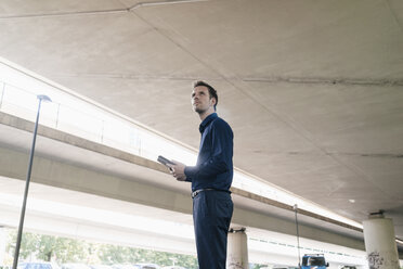 Businessman standing at underpass holding tablet - KNSF02485