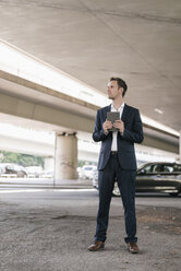 Businessman standing at underpass holding tablet - KNSF02502
