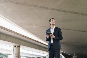 Businessman standing at underpass holding tablet - KNSF02503