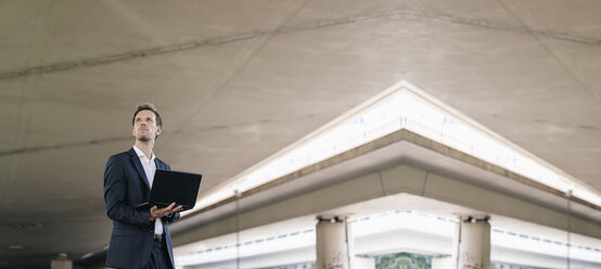 Businessman standing at underpass holding laptop, composite - KNSF02504