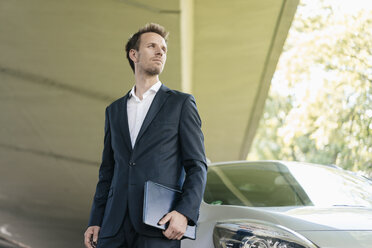 Businessman standing next to car holding laptop - KNSF02507