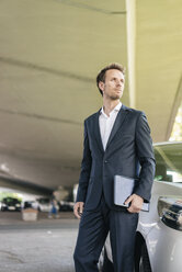 Businessman standing next to car holding laptop - KNSF02508