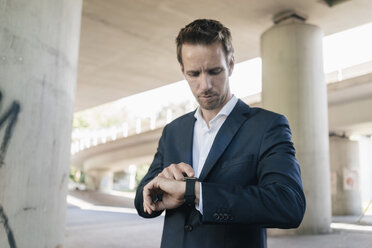 Businessman standing at underpass using smartwatch - KNSF02509