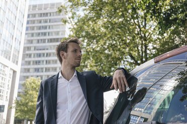 Businessman standing next to car with reflection of an office tower - KNSF02511