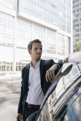 Businessman standing next to car with reflection of an office tower - KNSF02512