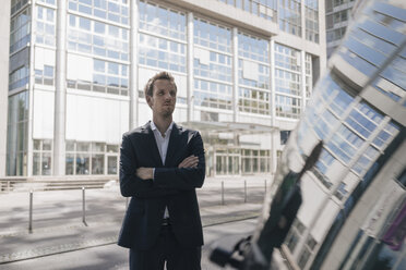 Businessman standing next to car with reflection of an office tower - KNSF02514