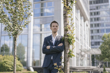 Geschäftsmann lehnt an einem Baum vor einem Bürogebäude - KNSF02516