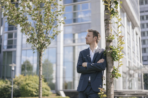 Geschäftsmann lehnt an einem Baum vor einem Bürogebäude, lizenzfreies Stockfoto