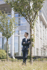 Geschäftsmann lehnt an einem Baum vor einem Bürogebäude - KNSF02518