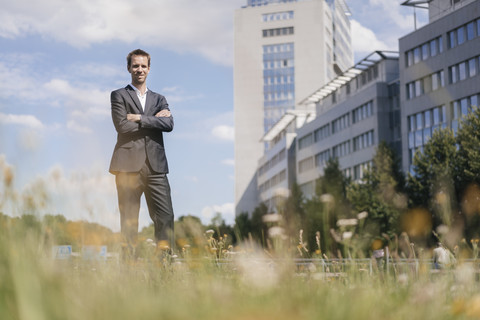 Geschäftsmann steht auf einem Feld vor einem Bürogebäude, lizenzfreies Stockfoto