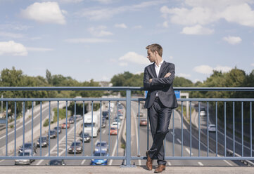 Geschäftsmann steht auf einer Brücke über einer Autobahn - KNSF02522