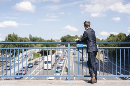 Geschäftsmann steht auf einer Brücke über einer Autobahn - KNSF02523