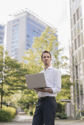 Businessman using laptop in front of office building - KNSF02531