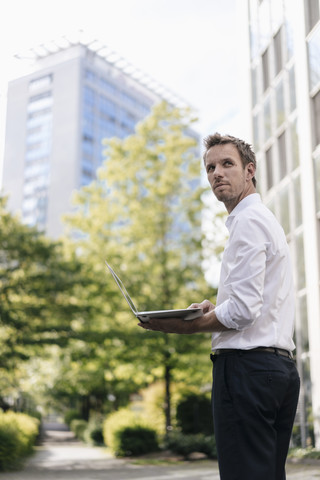 Geschäftsmann mit Laptop vor einem Bürogebäude, lizenzfreies Stockfoto