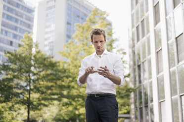 Businessman using portable glass device in front of office building - KNSF02536