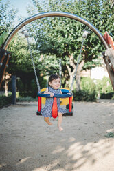 Happy baby girl sitting in swing on playground - GEMF01780