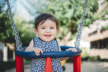Portrait of laughing baby girl sitting in swing on playground - GEMF01782