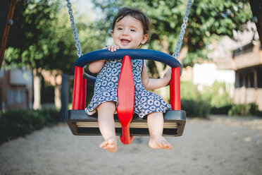 Portrait of laughing baby girl sitting in swing on playground - GEMF01783