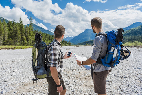 Germany, Bavaria, two hikers standing in dry creek bed orientating with cell phone and map - DIGF02791