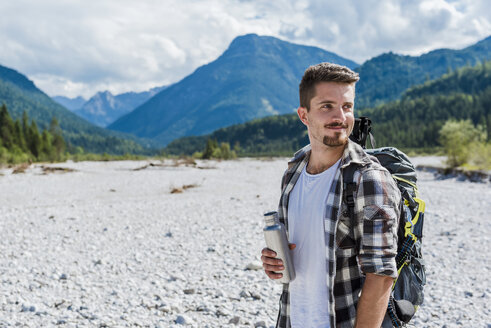 Germany, Bavaria, portrait of young hiker with backpack holding thermos flask - DIGF02796