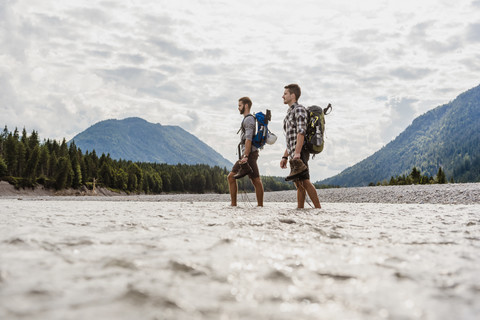 Deutschland, Bayern, zwei Wanderer mit Rucksäcken überqueren die Isar, lizenzfreies Stockfoto