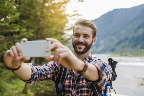 Porträt eines lächelnden jungen Wanderers, der ein Selfie mit seinem Handy macht - DIGF02820