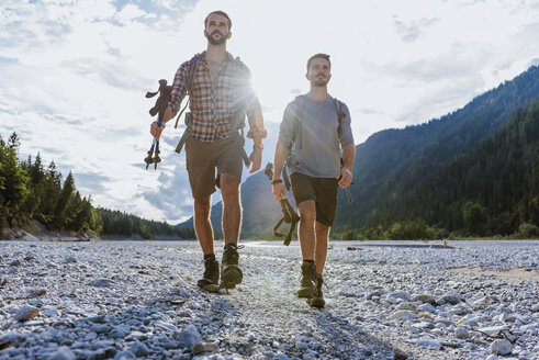 Germany, Bavaria, two hikers walking in dry creek bed at backlight - DIGF02823