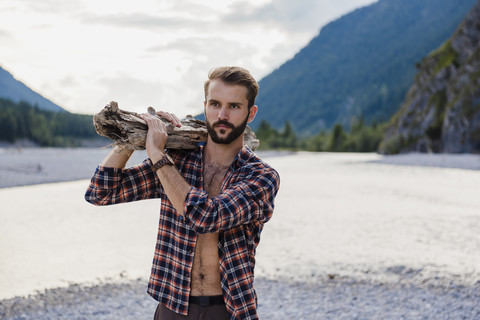 Germany, Bavaria, portrait of young man carrying firewood on his shoulder in nature stock photo