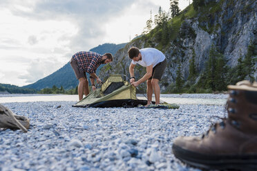 Germany, Bavaria, two hikers putting up tent on gravel bank - DIGF02828