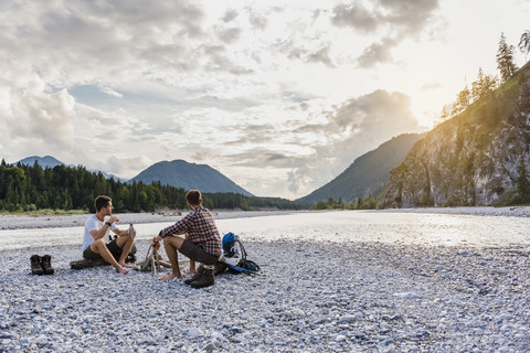 Deutschland, Bayern, zwei Wanderer, die sich abends auf einer Kiesbank ausruhen, lizenzfreies Stockfoto