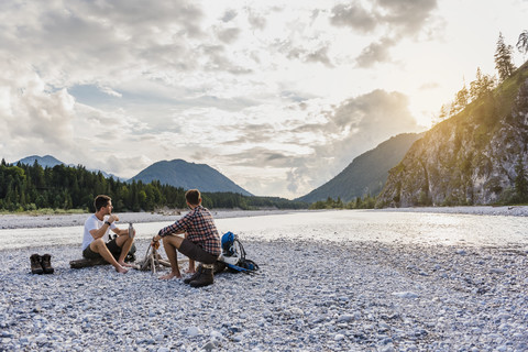 Germany, Bavaria, two hikers having a rest on gravel bank in the evening stock photo