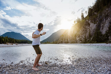 Germany, Bavaria, man standing at riverside throwing stone - DIGF02839