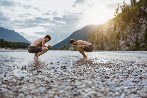 Germany, Bavaria, two friends washing their faces at riverside - DIGF02843