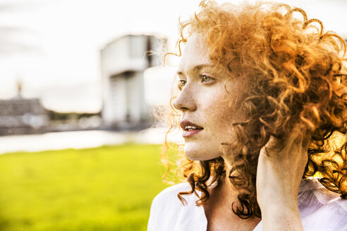 Deutschland, Köln, Porträt einer sommersprossigen jungen Frau mit lockigem rotem Haar - FMKF04383
