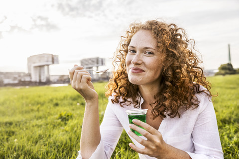 Germany, Cologne, portrait of happy young woman eating jelly on meadow stock photo
