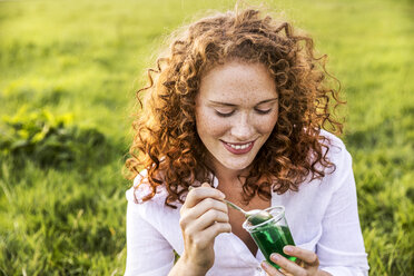Portrait of smiling young woman eating jelly on meadow - FMKF04388