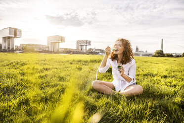 Germany, Cologne, portrait of happy young woman eating jelly on meadow - FMKF04389