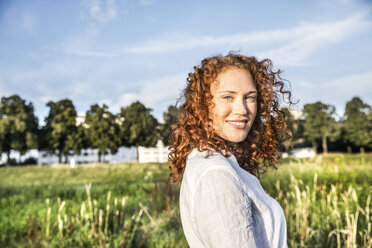 Germany, Cologne, portrait of smiling young woman with curly red hair in nature - FMKF04391