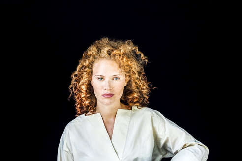 Portrait of serious young woman with curly red hair in front of black background - FMKF04402