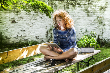 Porträt einer jungen Frau, die am Biertisch im Garten sitzt und ein Tablet benutzt - FMKF04414