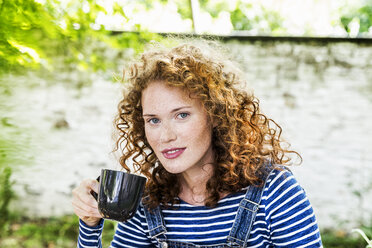Deutschland, Köln, Porträt einer sommersprossigen jungen Frau mit einer Tasse Kaffee - FMKF04415