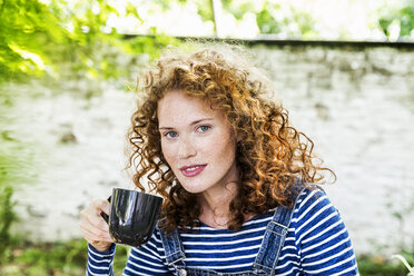 Germany, Cologne, portrait of freckled young woman with cup of coffee - FMKF04415