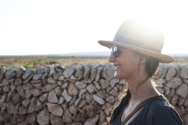 Spain, Menorca, happy single traveller wearing straw hat and sunglasses at backlight - IGGF00146