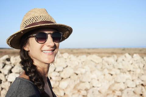 Spanien, Menorca, Porträt einer lächelnden Frau mit Strohhut und Sonnenbrille, lizenzfreies Stockfoto