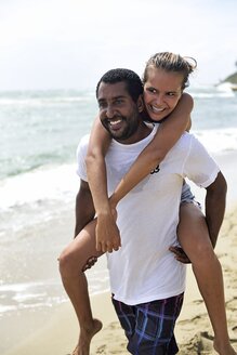 Mann nimmt seine Freundin am Strand huckepack - ECPF00083
