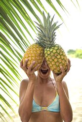 Junge Frau hält zwei Ananas an einer Palme - ECPF00099