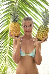 Junge Frau hält zwei Ananas an einer Palme - ECPF00101