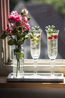 Zwei Champagnergläser mit Maiwein und Himbeeren auf der Fensterbank - SBDF03300